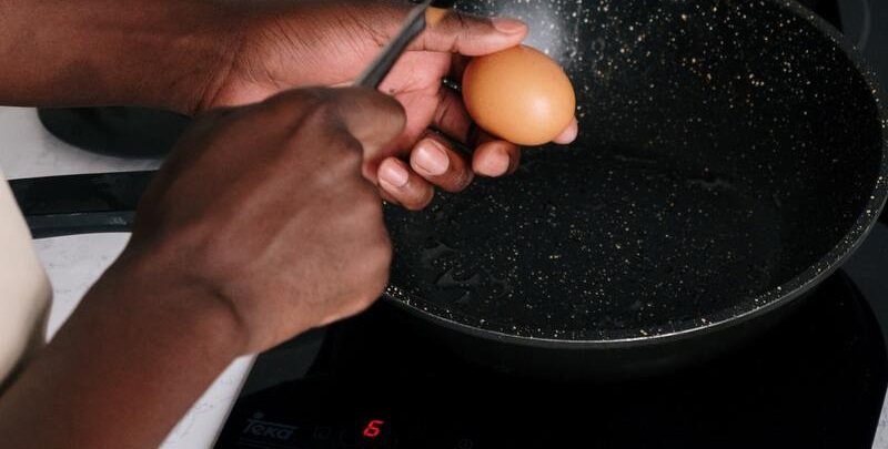 Person breaking an egg on a frying pan sitting on electric cooktop