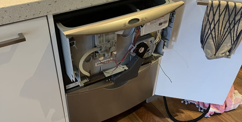 Installed dishwasher with wiring and controls exposed.
